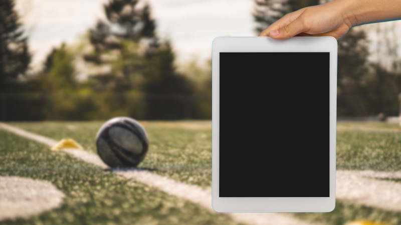 A Tablet Held in Front of A Soccer Field with A Ball in The Background